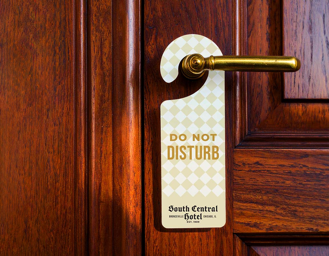 A hotel do-not-disturb hang tag attached to a brass door handle on a dark wood door. The tag is cream with a subtle diamond pattern and gold text reading 'DO NOT DISTURB' and 'South Central Hotel London Ct.