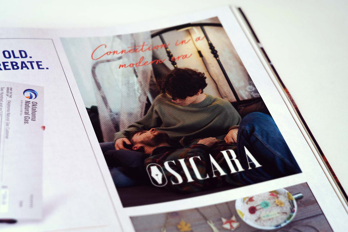 A printed magazine or brochure page featuring a large photo of a couple with the text 'Connection in a modern era' and 'SICARA' across the bottom. The page is photographed at an angle on a white surface, with part of another printed page visible on the left.