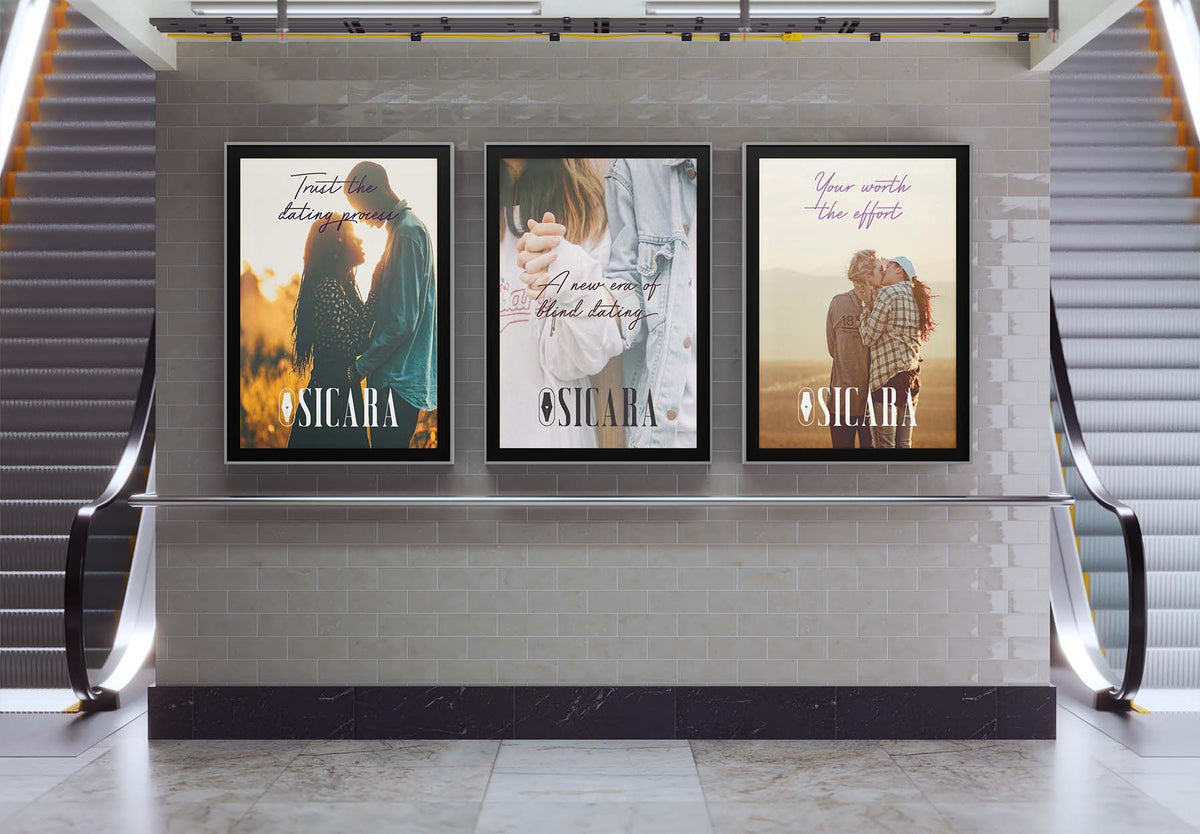 Three framed vertical posters with the brand name “SICARA” displayed on a light gray brick wall between escalators in a modern indoor setting.