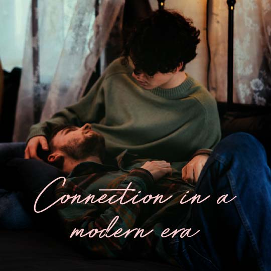 A man in a muted green sweater sits closely with another man lying down in a dim indoor setting, with the overlaid text 'Connection in a modern era' in white script across the lower portion.