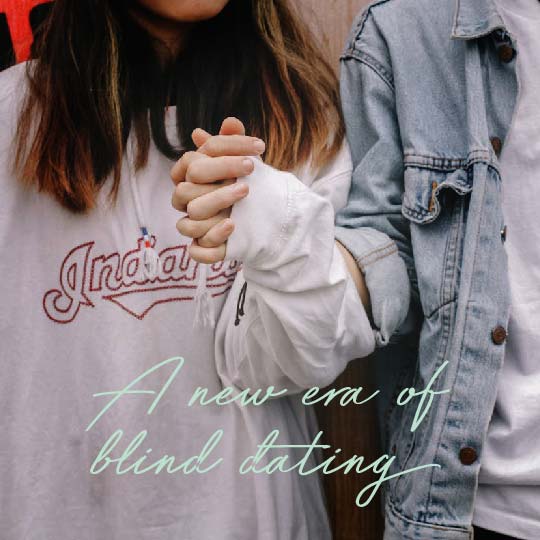 Two people holding hands, one wearing a white sweatshirt with red script text and the other wearing a light blue denim jacket over a white shirt. The text 'A new era of blind dating' is overlaid across the bottom.